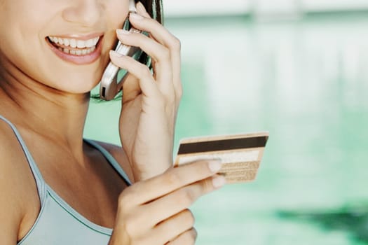 Close-up of a young woman holding a credit card and talking on a mobile phone