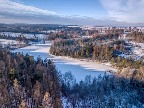 Aerial bird view of beautiful winter landscape with frozen water reservoir situated in forest covered with snow. European countryside. Czech Republic, Vysocina Highland region, Europe