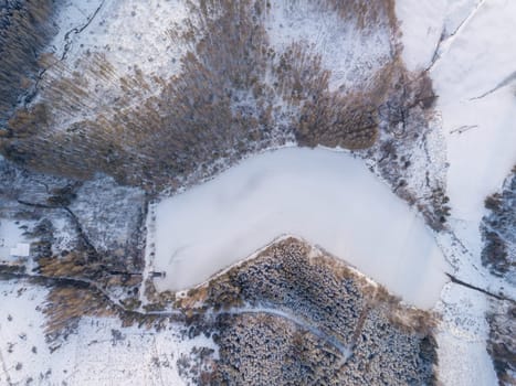 Aerial bird eye view of beautiful winter landscape with frozen water reservoir situated in forest covered with snow. European countryside. Czech Republic, Vysocina Highland region, Europe