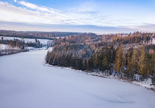 Aerial bird view of beautiful winter landscape with frozen water reservoir situated in forest covered with snow. European countryside. Czech Republic, Vysocina Highland region, Europe