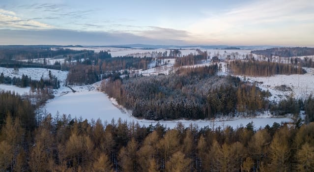 Aerial bird view of beautiful winter landscape with frozen water reservoir situated in forest covered with snow. European countryside. Czech Republic, Vysocina Highland region, Europe