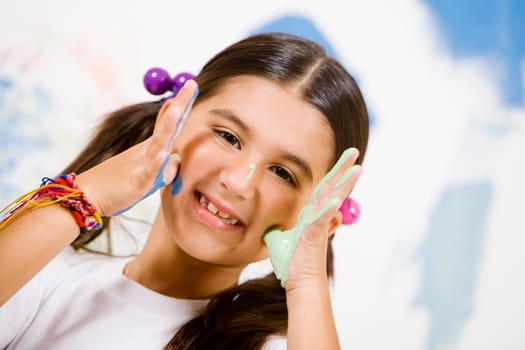 Portrait of a girl with paint on her palms and touching her cheeks