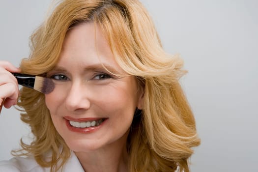 Portrait of a mature woman applying blush on her cheek and smiling