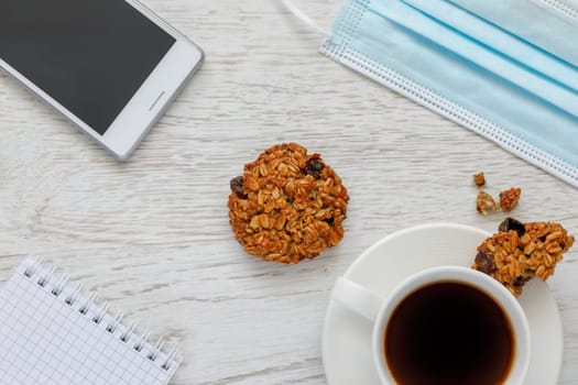 Background with coffee, cookies, notepad and medical mask, top view