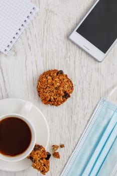 Background with coffee, cookies, notepad and medical mask, top view