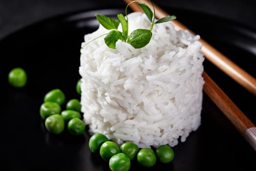 Garnish of white long rice with green peas and green sprouts on a dark background with Chinese chopsticks