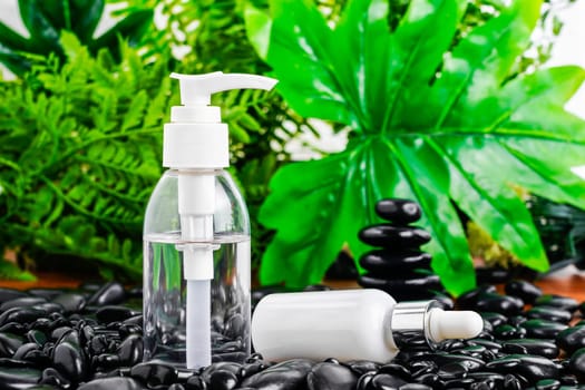 Thai Spa massage setting with serum oil bottle dropper mock up or essential oil on black stone against green leave background
