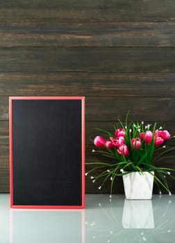 Flower vase and blank chalkboard on table near wood background