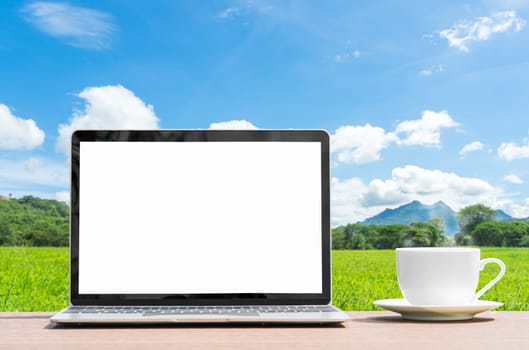 laptop and cofree cup on table agent green grass field in countryside