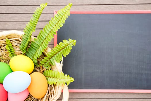 Colorful easter eggs in the basket and blackboard on wood background with space