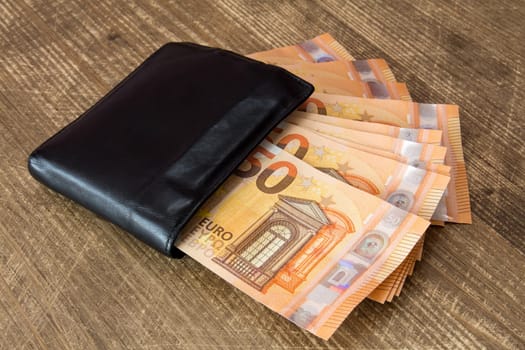 Money in black leather wallet on wooden background