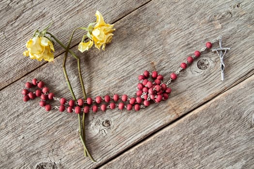 Catholic rosary and dry yellow roses on wooden background