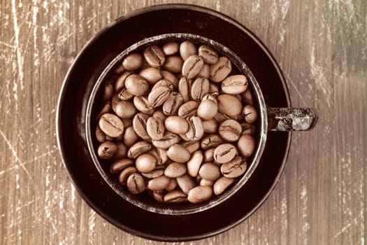 Coffee cup full of coffee beans on old wooden background.