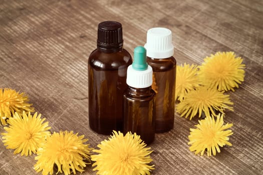 Dandelion extract in a small bottles with yellow flowers on wooden background