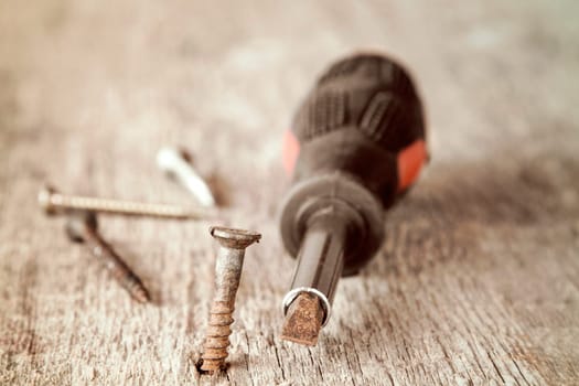 Old screwdriver and rusty screws on the wooden plank