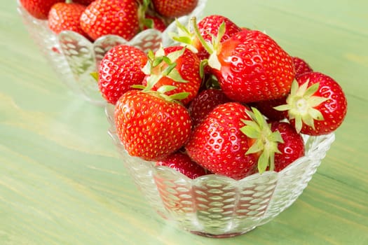 Glass bowls with red strawberries on wooden background