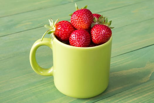 Green mug with strawberries on a wooden background