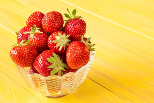 Glass bowl full of red strawberries on yellow wooden background