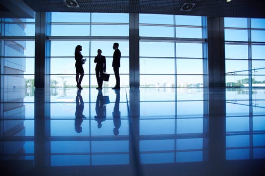 Silhouettes of group of office workers standing by the window and talking