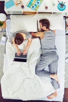 Woman using laptop in bed whiles her boyfriend sleeping