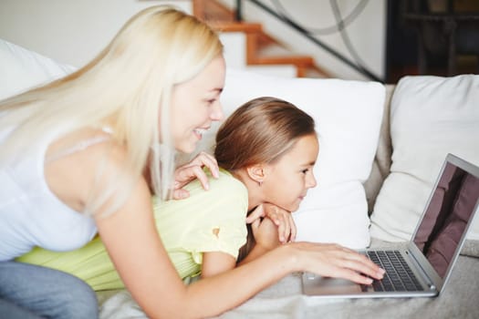 Pretty mother and daughter sitting on sofa and looking at computer