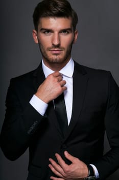 Bearded young businessman in a stylish suit tie with sunglasses a serious thoughtful expression against a grey background in the portrait
