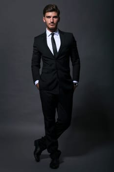 Bearded young businessman in a stylish suit tie with sunglasses a serious thoughtful expression against a grey background in the portrait