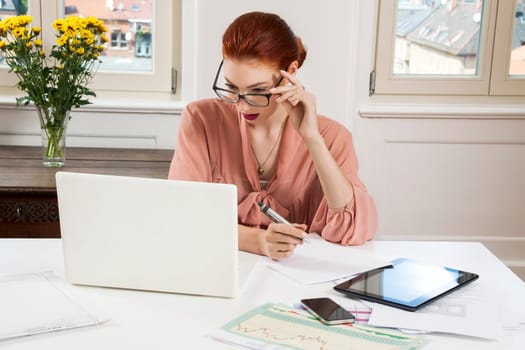 Young businesswoman reads statistics at the desk on the computer with red hair and glasses in the office
