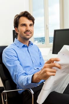 Young businessman sits with documents at a grater table in the office and informs himself