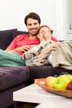 Young couple in the living room on the couch while reading and watching TV at home