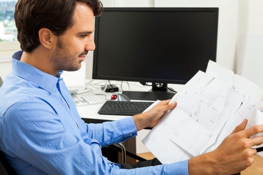 Young businessman sits with documents at a grater table in the office and informs himself