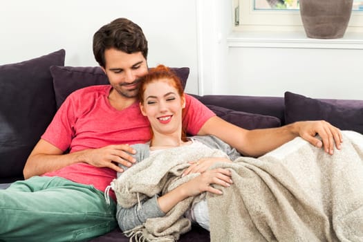Young couple in the living room on the couch while reading and watching TV at home