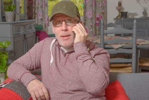 a senior with a phone sitting on the sofa in his house