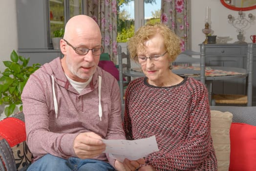 a mother and her adult son looking paper on a sofa