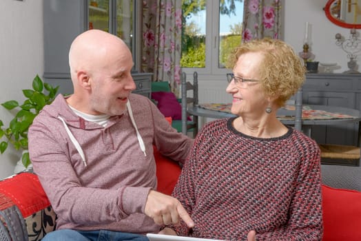 a mother and her adult son looking at a digital tablet