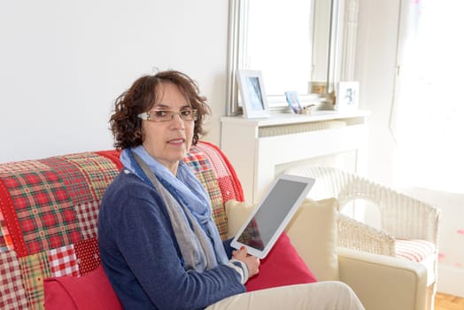 a middle aged woman smiling with a digital tablet on her sofa