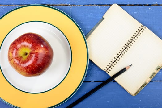 Apple and notebook with pencil on a blue table