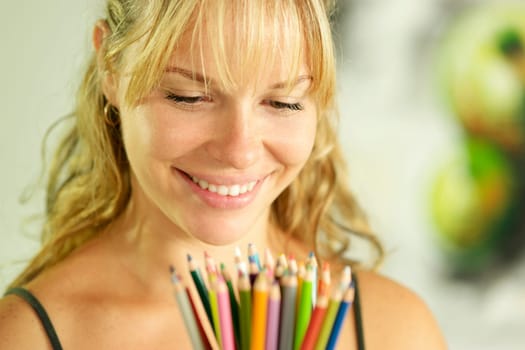 Portrait of young woman holding bunch of colorful pencils at camera and smiling
