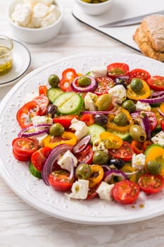 Greek salad of fresh cucumber, tomato, sweet pepper, lettuce, red onion, feta cheese and olives with olive oil dressing. Healthy food