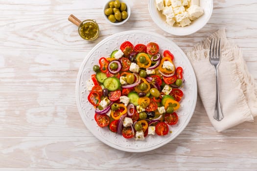 Greek salad of fresh cucumber, tomato, sweet pepper, lettuce, red onion, feta cheese and olives with olive oil dressing. Healthy food, top view
