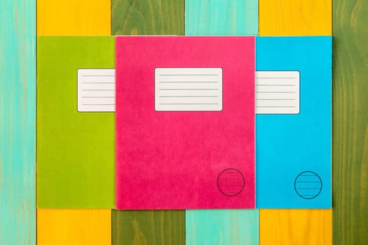 Three  exercise books on the colorful wooden background