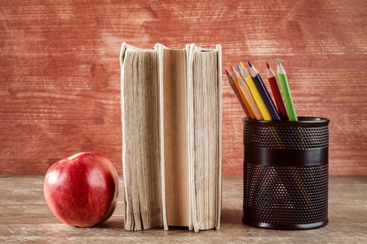 Books,apple and pencil cup on wooden background