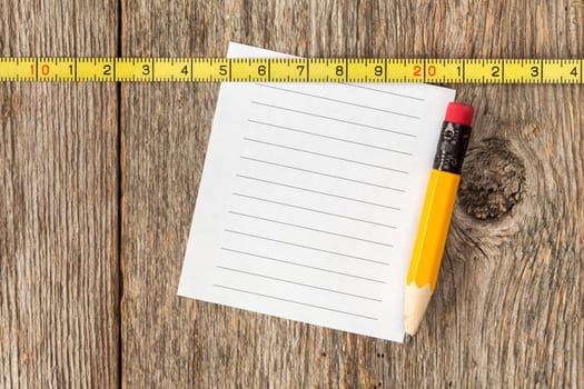 Blank note paper,pencil and tape measure on wooden texture