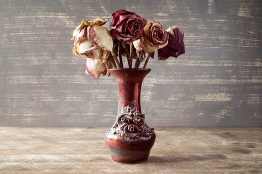 Bouquet of dry roses in a vase on wooden background