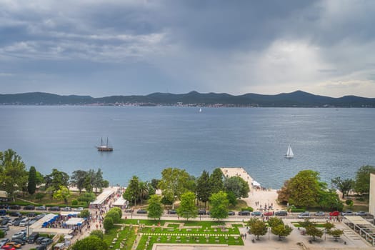 Drone or aerial view on crowds of tourists visiting a market on the pier in old town district of Zadar with sailboats sailing on Adriatic Sea, Croatia