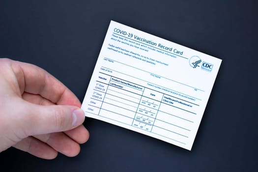 Calgary, Alberta. Canada. Feb 3, 2021. A person holding a COVID-19 Vaccination record card on a black background.