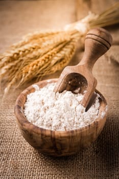Flour in wooden bowl with grain on burlap background