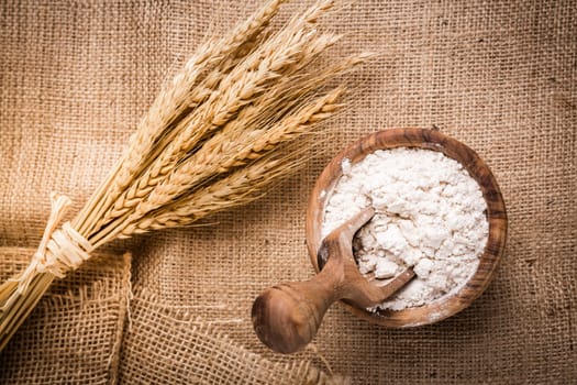 Flour in wooden bowl with grain on burlap background