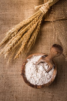 Flour in wooden bowl with grain on burlap background