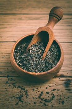 Dried black tea leaves in bowl on wooden background